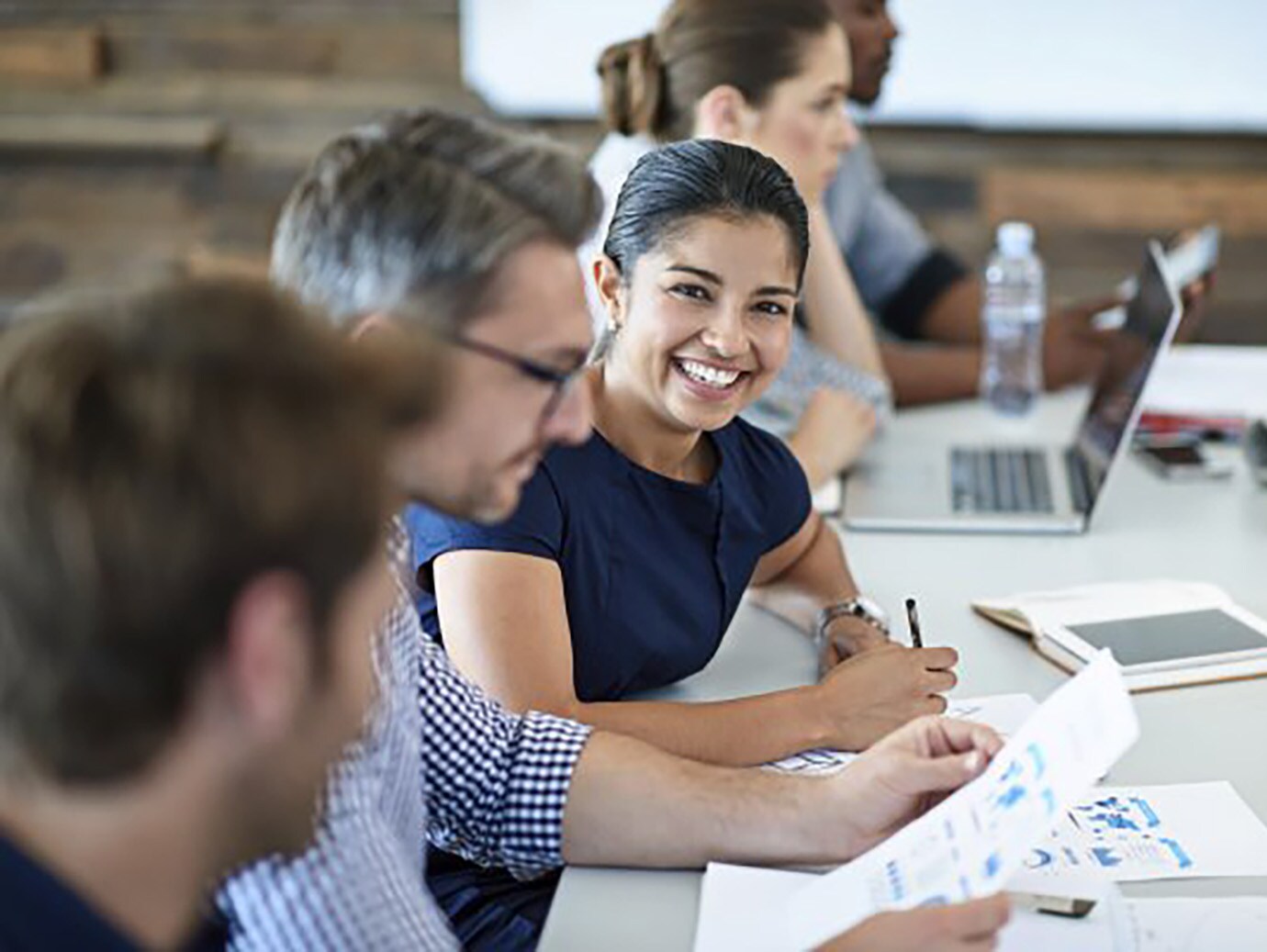 Woman smiling at the camera during a meeting while sitting amongst a group of people